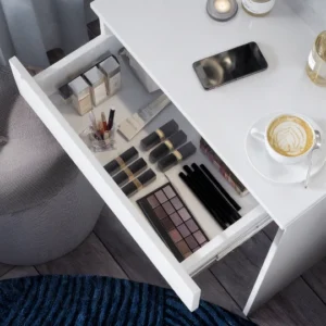 Вид зверху на відкриту білу шухляду туалетного столика, що містить різноманітну косметику, таку як флакони тонального крему, помади, палітра тіней для повік і пензлі для макіяжу.